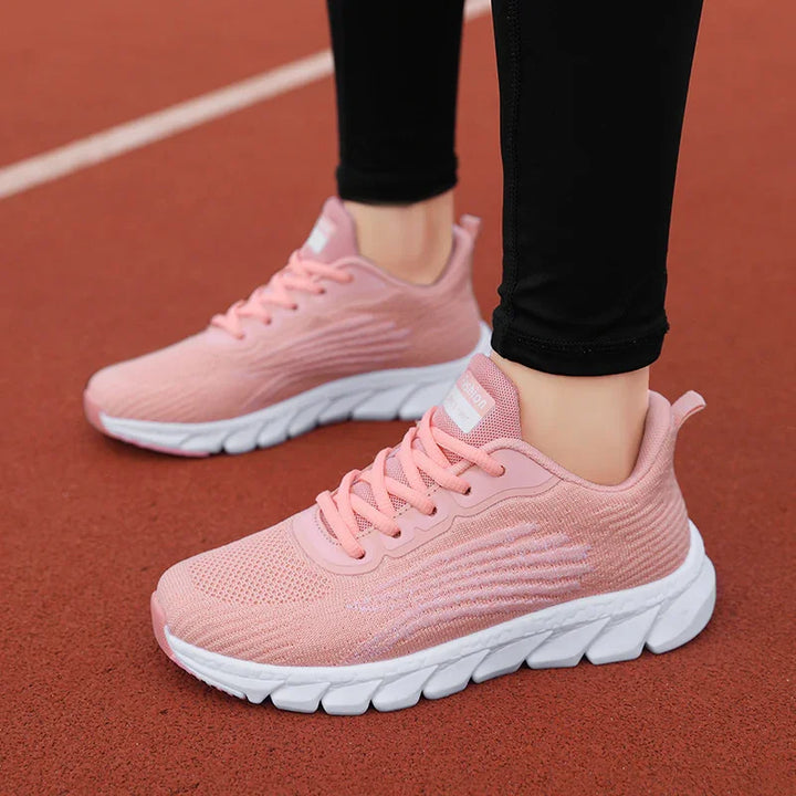 Pink lightweight running shoes with white soles worn with black leggings on red track