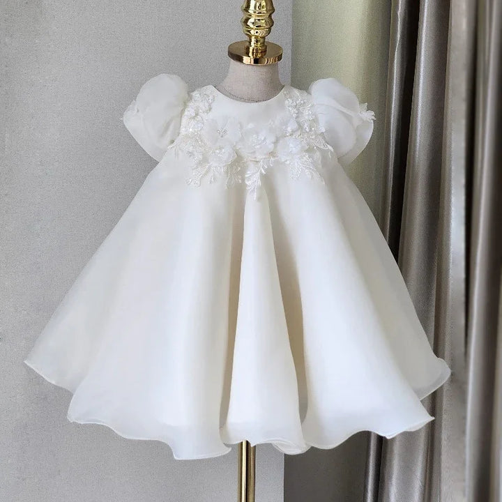 White baby dress with puff sleeves and floral lace appliqué on bodice displayed on mannequin