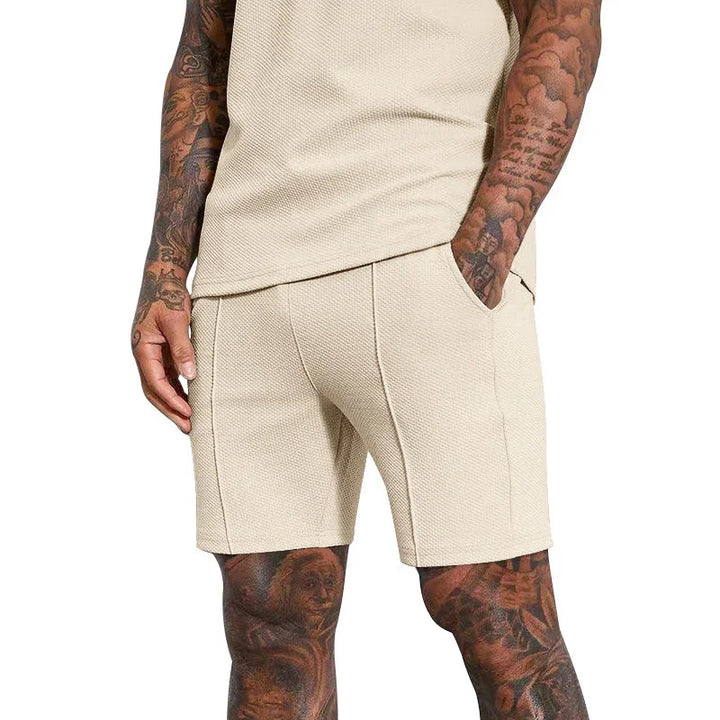 Man wearing beige textured shorts and matching sleeveless top, showing tattooed arms and legs