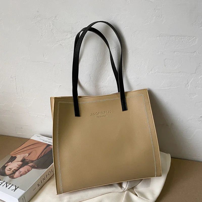 Beige JINGPINPIJU Fashion tote bag with black handles on white cloth, next to Kinfolk magazine