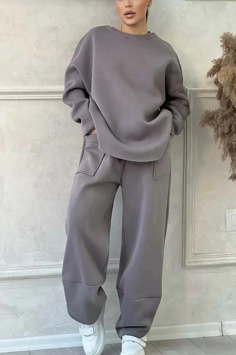 Woman wearing oversized grey sweatshirt and matching wide-leg pants with white sneakers in minimalist room