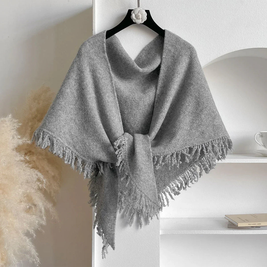 Cozy gray fringed woolen shawl hanging on a black hanger with white flower, neutral decor background