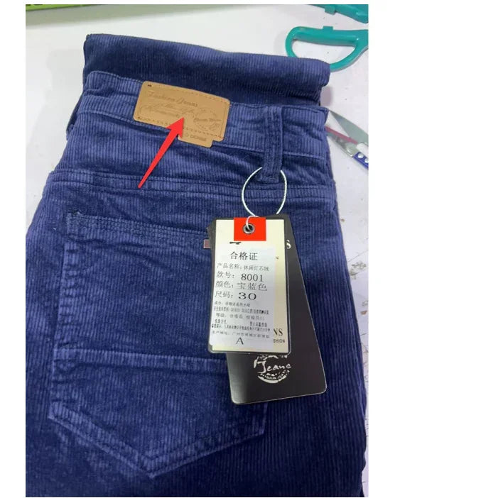 Blue corduroy jeans with back pocket, leather brand patch, and hanging size tags on white surface