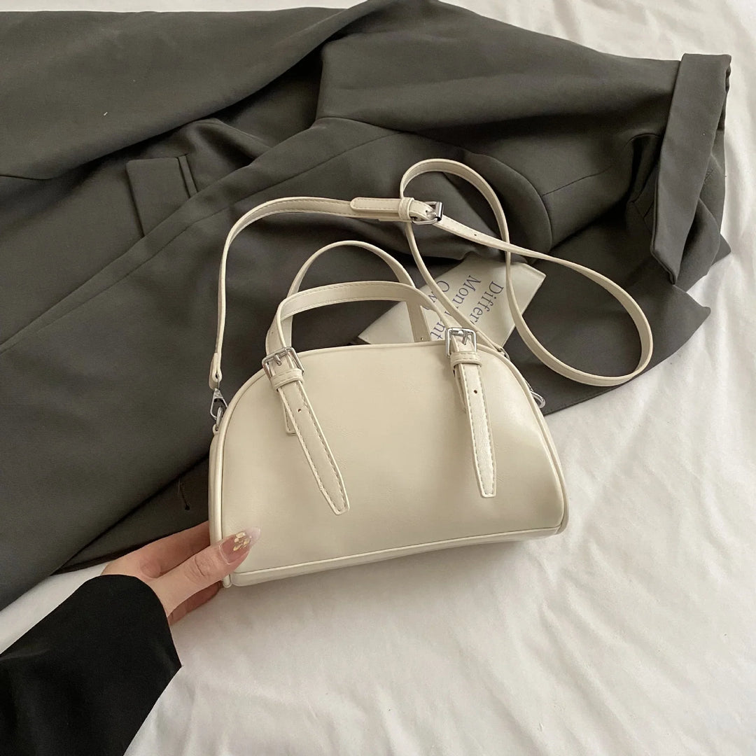 Cream-colored small handbag with double buckle straps on dark gray blazer and white fabric