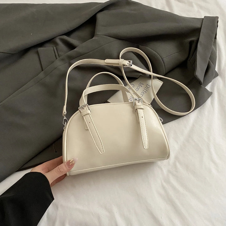 Cream-colored small handbag with double buckle straps on dark gray blazer and white fabric