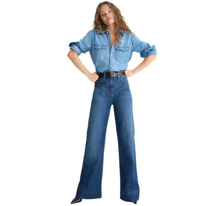 Woman wearing light blue denim shirt and high-waisted wide-leg jeans with black belt on white background