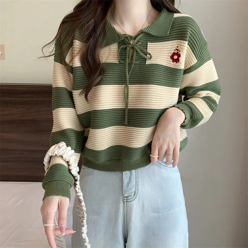 Woman wearing green and beige striped knit sweater with collar and floral embroidery, paired with light blue jeans