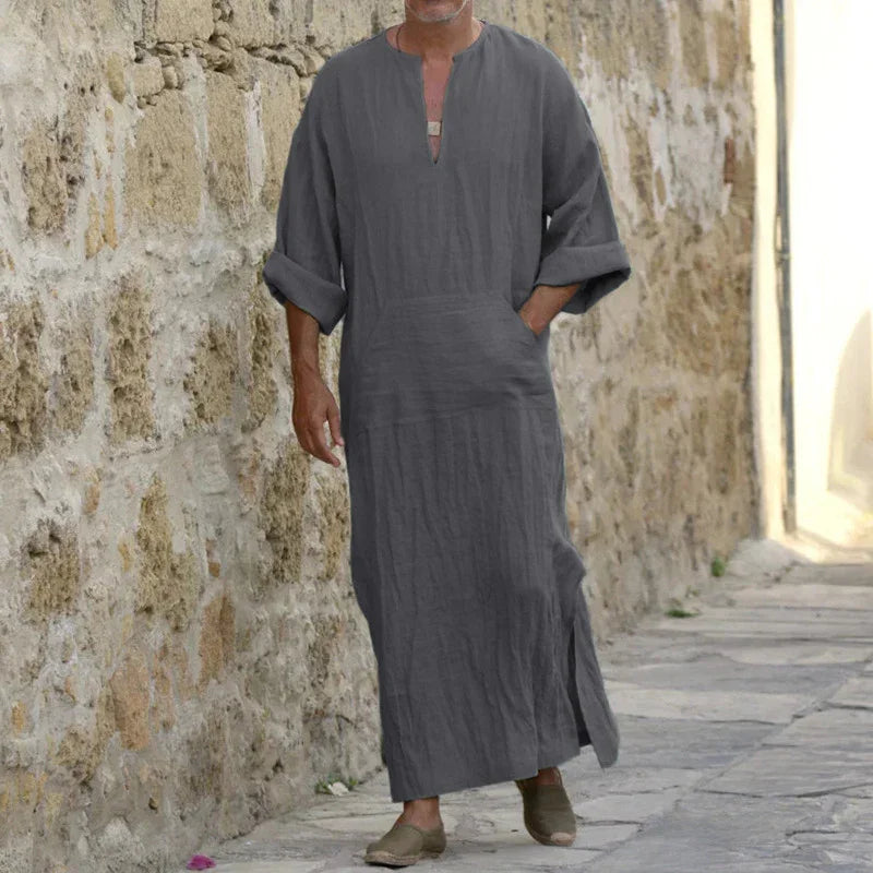 Man walking in gray long linen robe with rolled sleeves and side slits on stone pathway