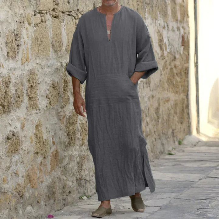 Man walking in gray long linen robe with rolled sleeves and side slits on stone pathway