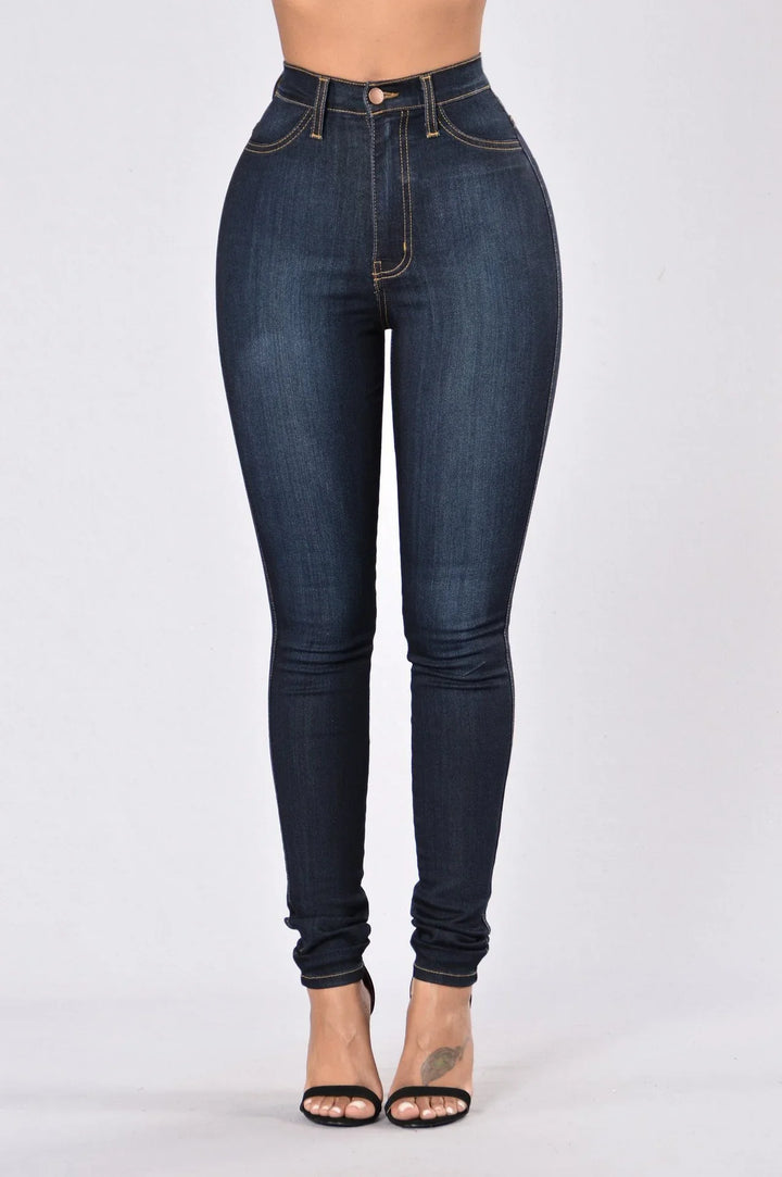 High-waisted dark blue skinny jeans on a model with black open-toe heels, minimal background