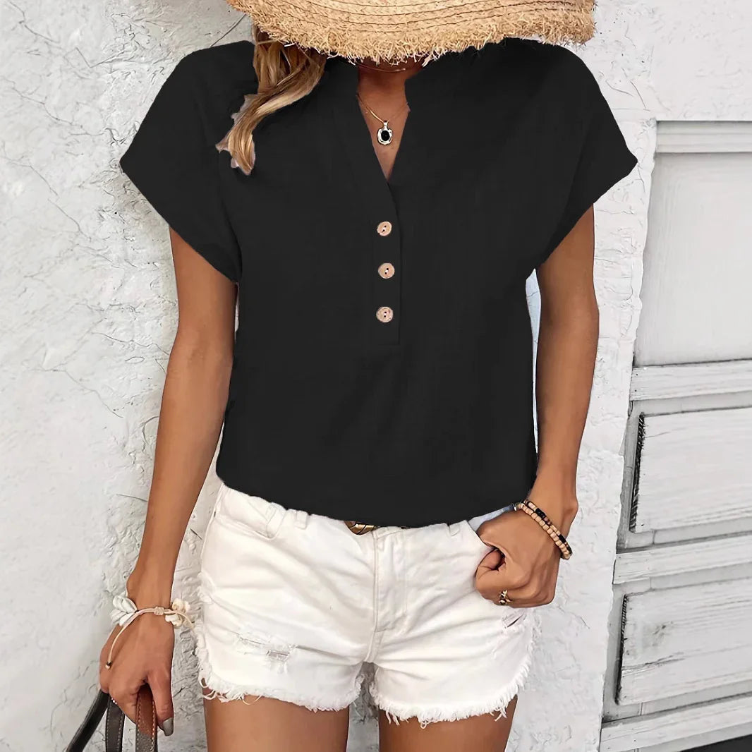 Woman wearing black buttoned short-sleeve top with white ripped denim shorts and straw hat