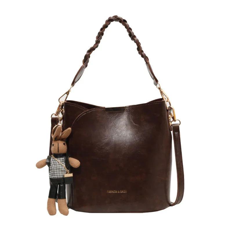 Dark brown leather bucket bag with braided handle and attached knitted bunny keychain