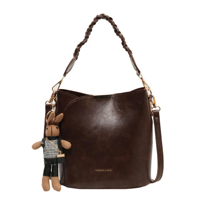 Dark brown leather bucket bag with braided handle and attached knitted bunny keychain