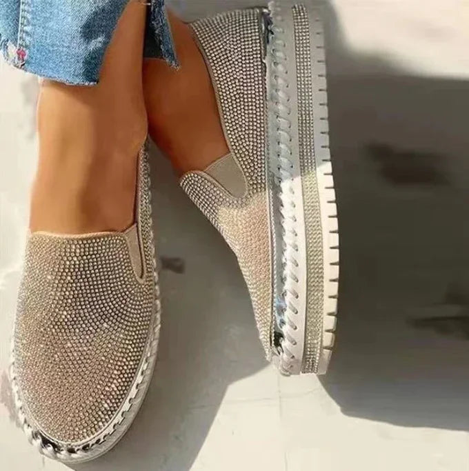 Women's sparkling rhinestone slip-on sneakers with thick white soles, worn with cropped denim jeans