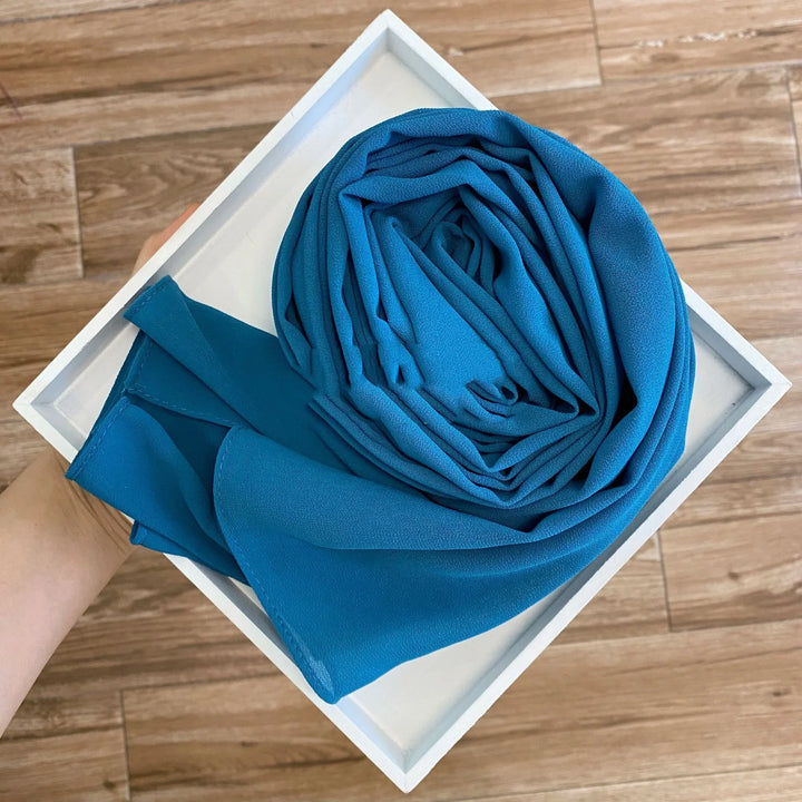 Hand holding white tray with neatly folded bright blue fabric on wooden floor background