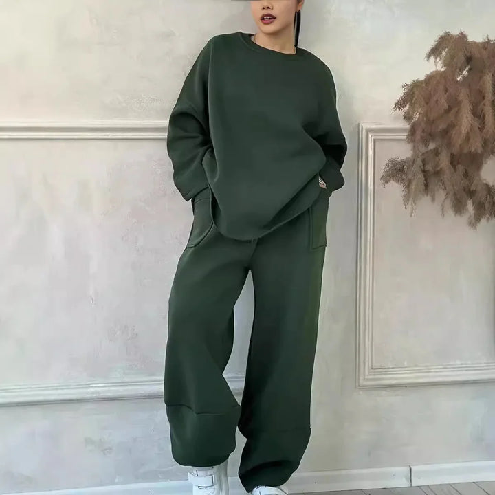 Woman wearing dark green oversized sweatshirt and pants with white sneakers standing indoors