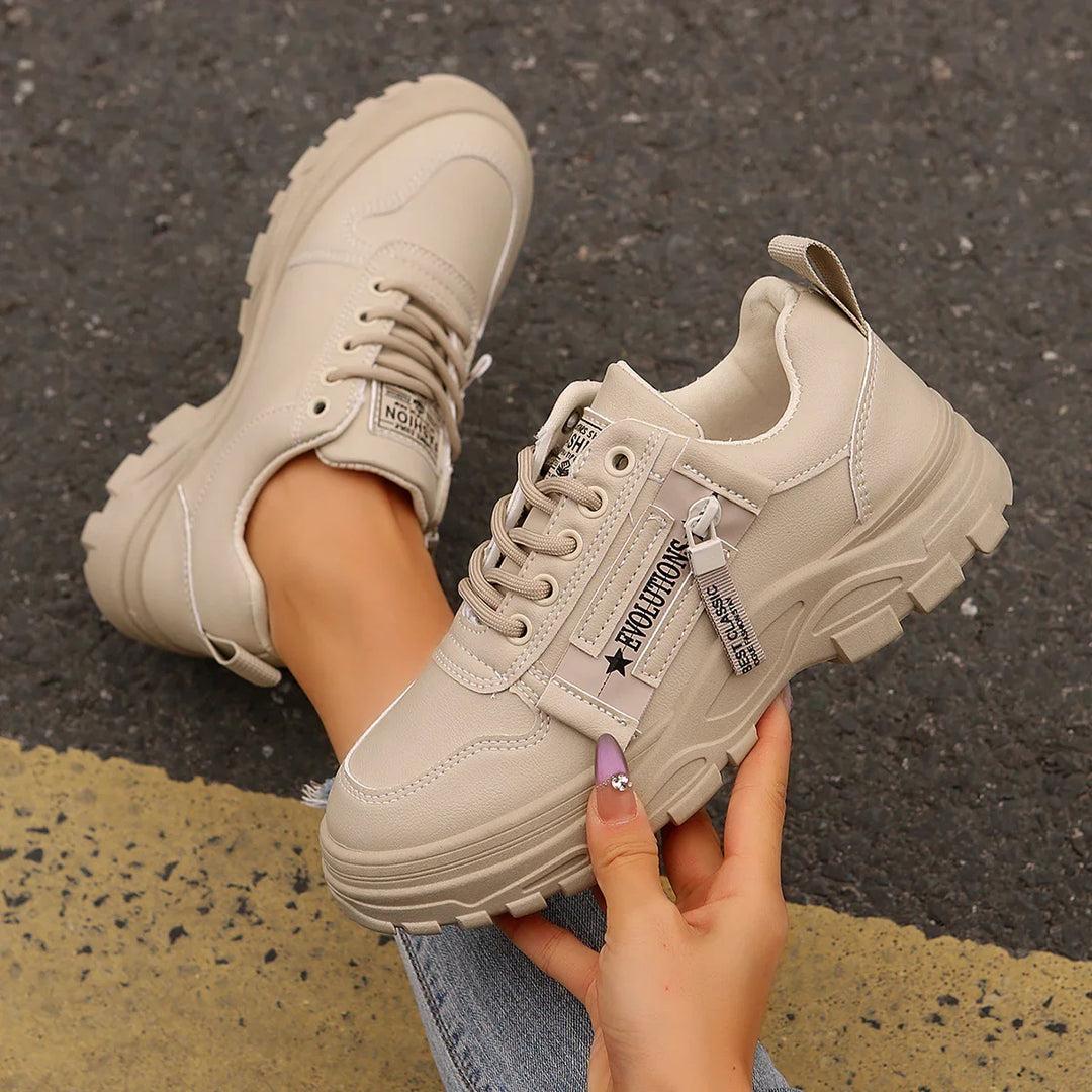 Beige chunky platform sneakers with zipper detail worn on asphalt with yellow line
