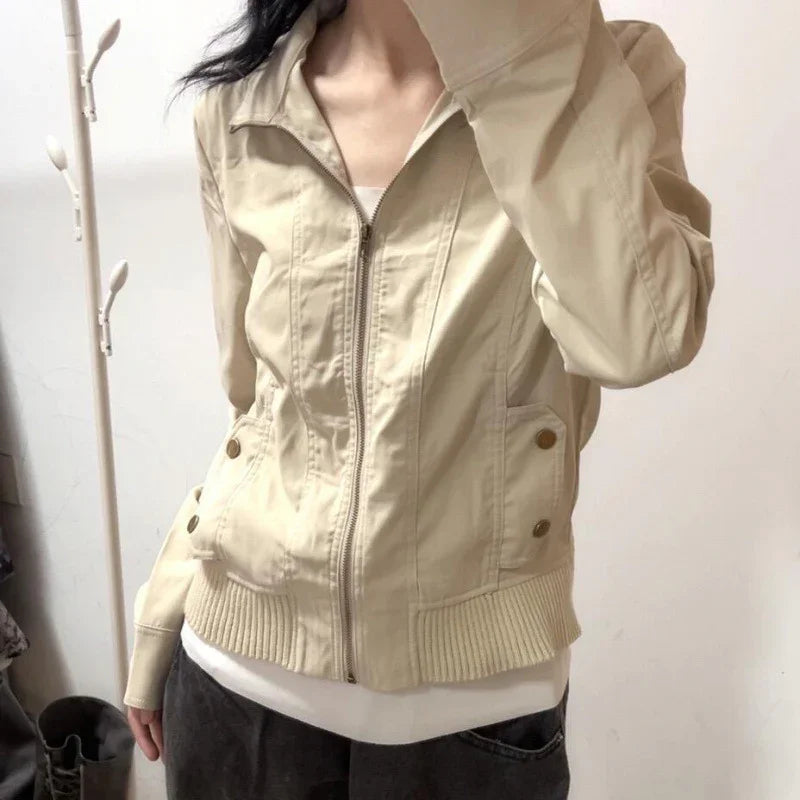 Woman wearing beige zip-up jacket with ribbed hem and buttoned pockets indoors