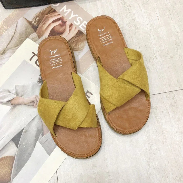 Yellow suede cross strap sandals on a tiled floor with fashion magazine background