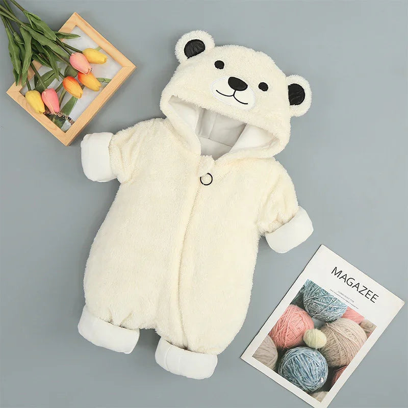 White baby romper with bear face hood, soft fleece fabric, laid flat on gray surface with flowers and magazine
