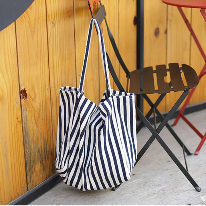 Striped navy blue and white canvas tote bag hanging on black metal chair in outdoor wooden patio setting