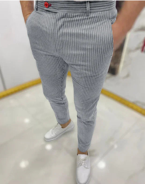 Men's slim fit gray pinstripe trousers paired with white lace-up shoes in a modern indoor setting