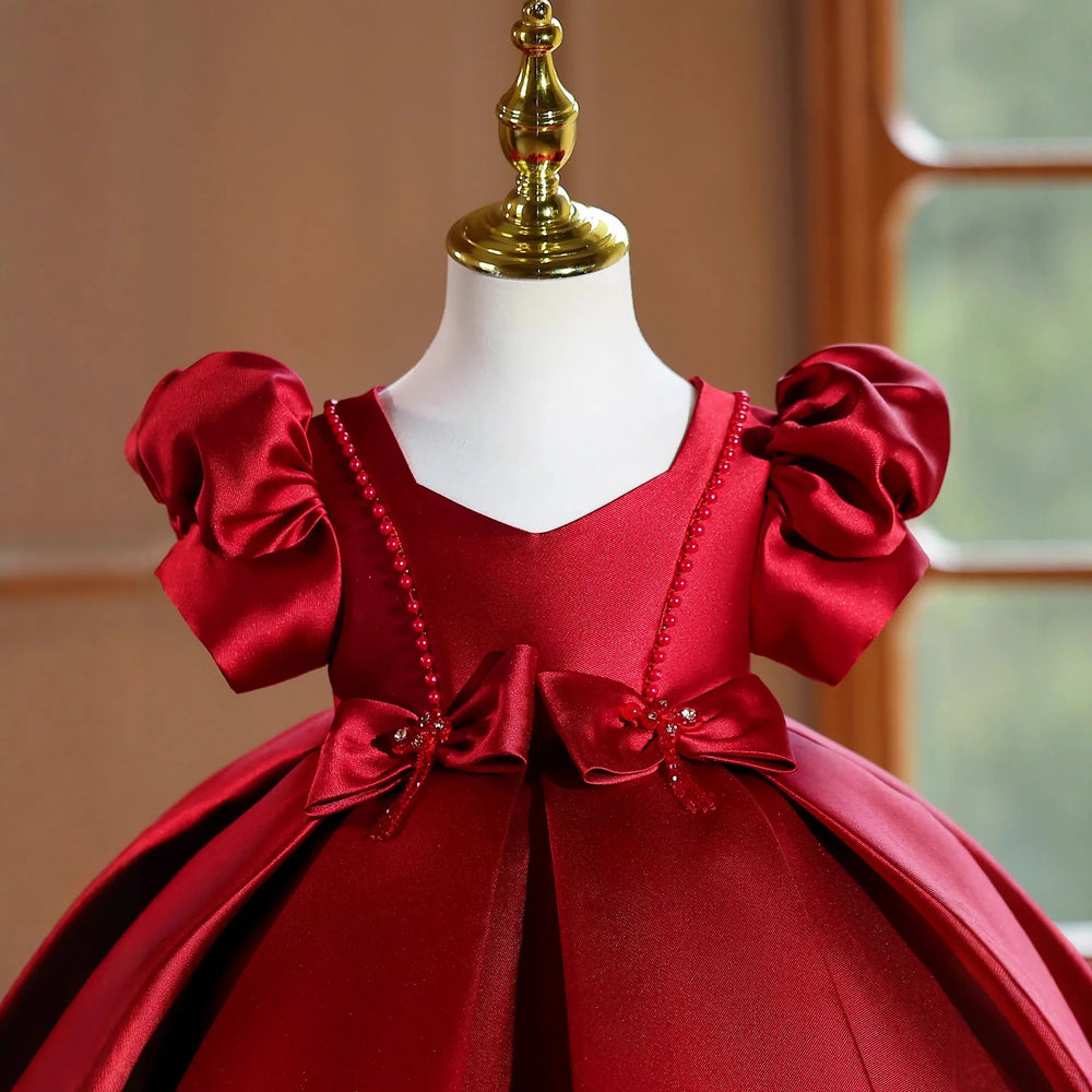 Elegant red satin baby dress with puff sleeves and bow details on mannequin