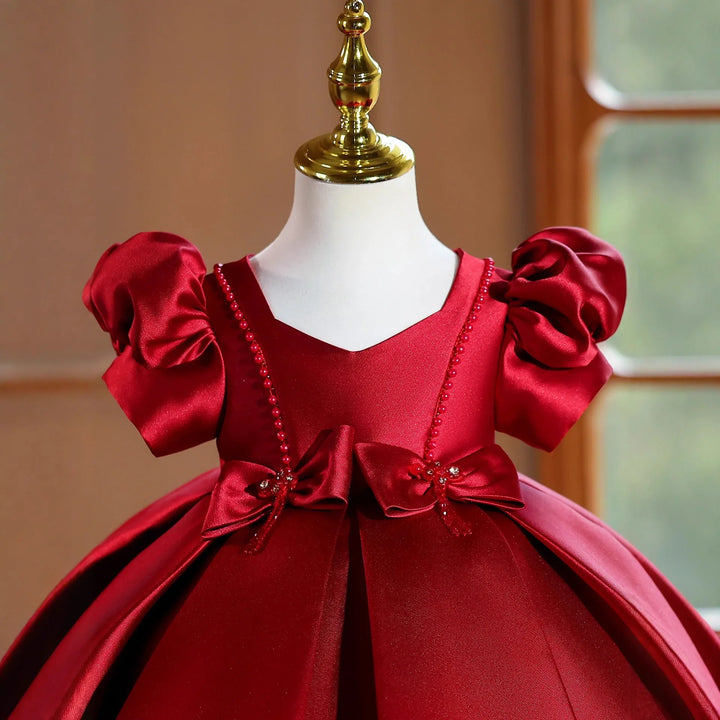 Elegant red satin baby dress with puff sleeves and bow details on mannequin