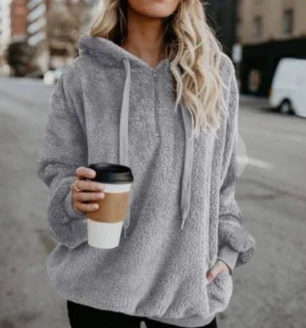 Woman wearing cozy gray sherpa hoodie holding coffee cup outdoors in urban setting