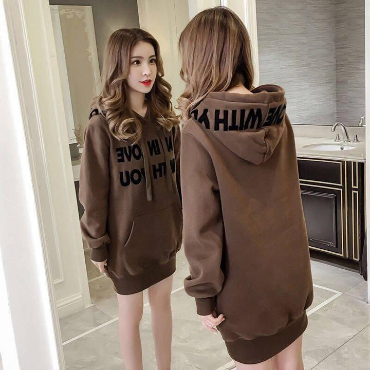 Woman wearing brown oversized hoodie dress with front pocket, standing in a modern bathroom near mirror