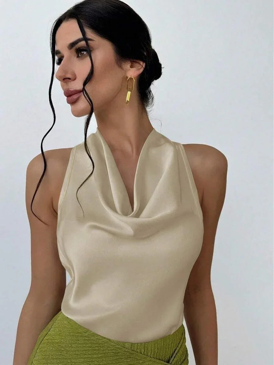 Woman with dark hair in a silky cream sleeveless top and green textured skirt with gold earrings