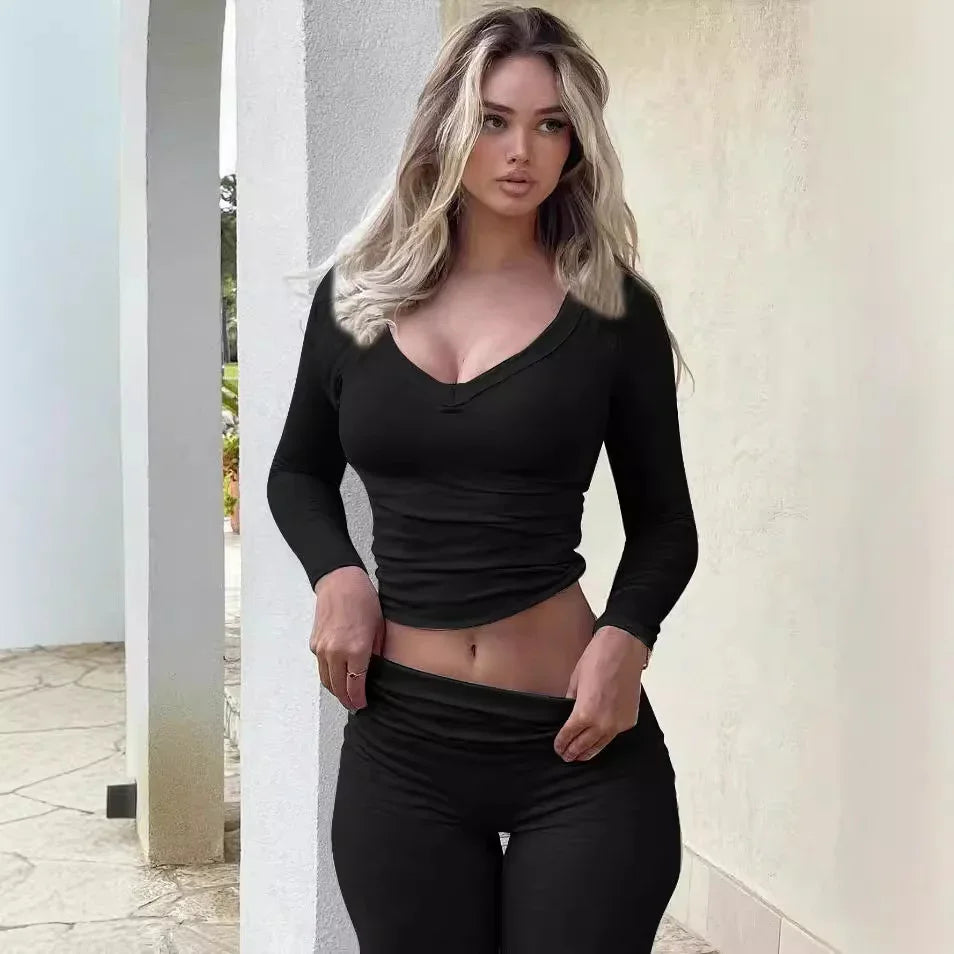 Woman in black long-sleeve crop top and leggings posing against white stucco wall outdoors