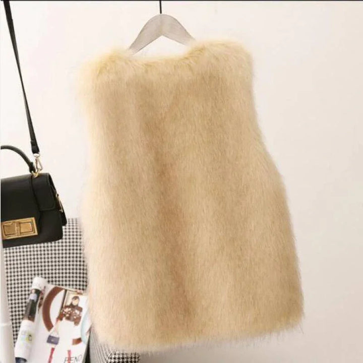 Beige fuzzy faux fur vest hanging on wooden hanger with black handbag and fashion magazine nearby