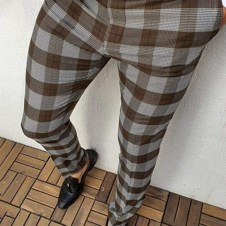 Person wearing brown and gray plaid fitted pants with black loafers on wooden floor
