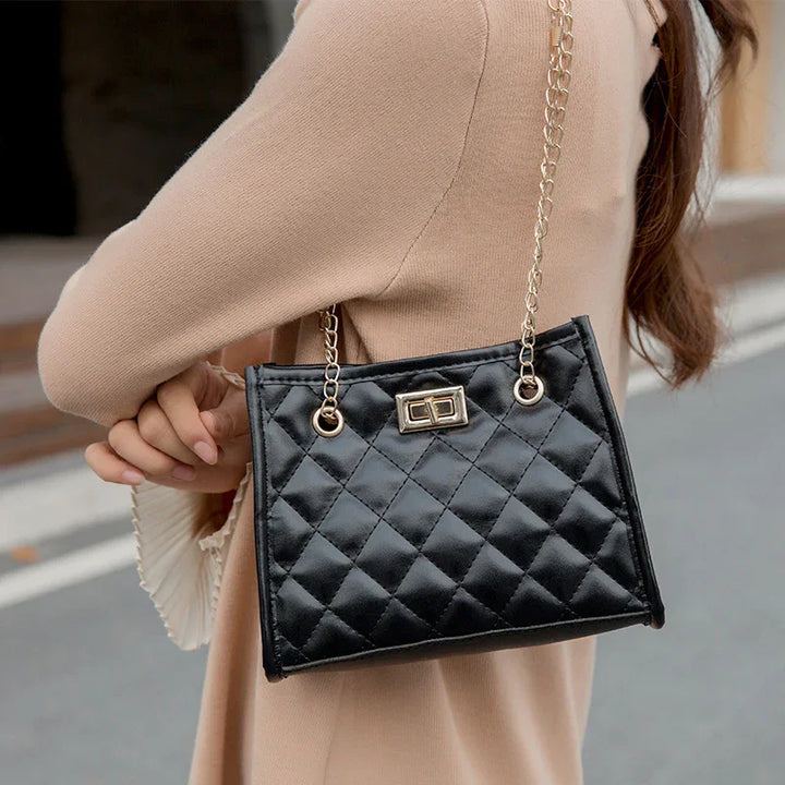 Woman wearing beige coat carrying stylish black quilted handbag with gold chain strap outdoors