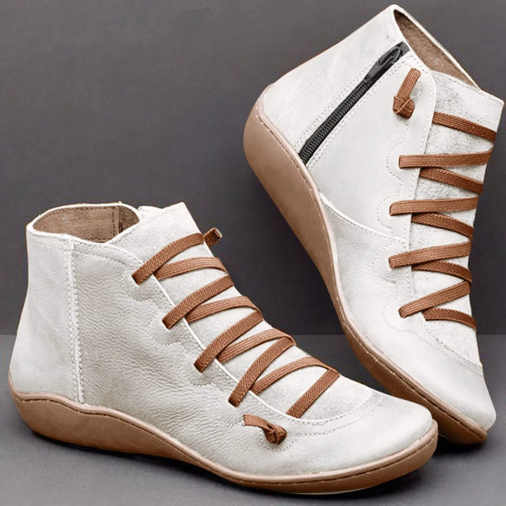White leather ankle boots with brown laces and beige soles on gray background