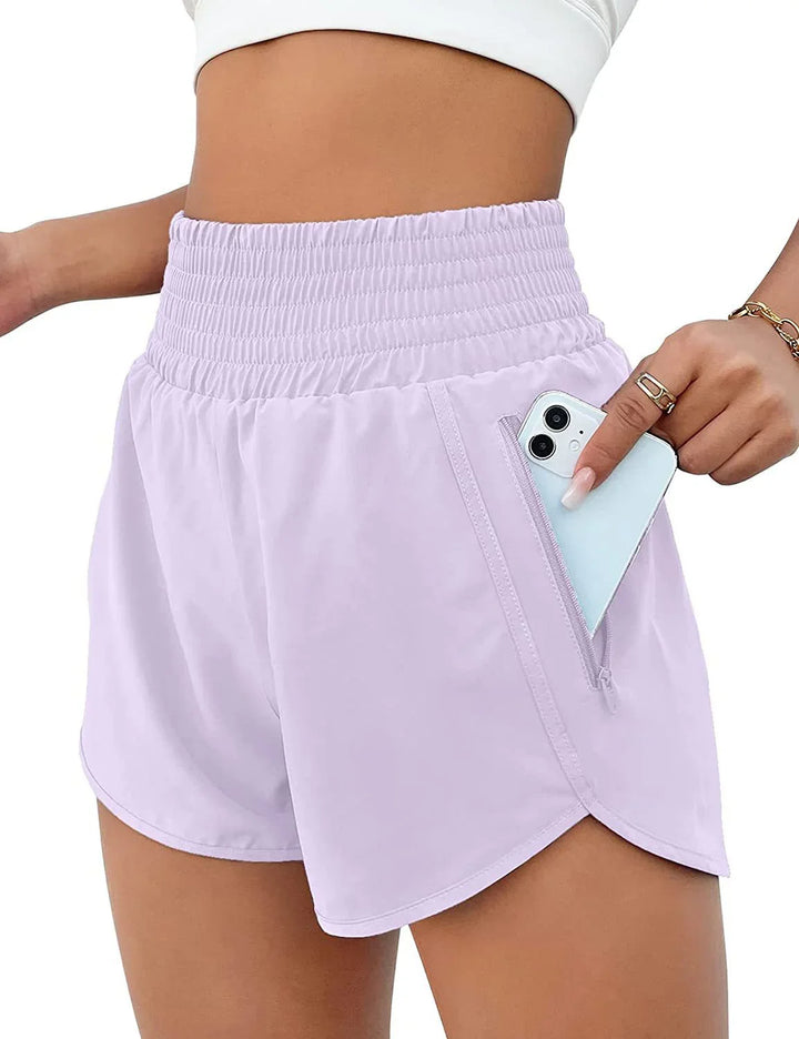 Woman wearing light purple high-waisted athletic shorts with side zipper pocket holding a smartphone