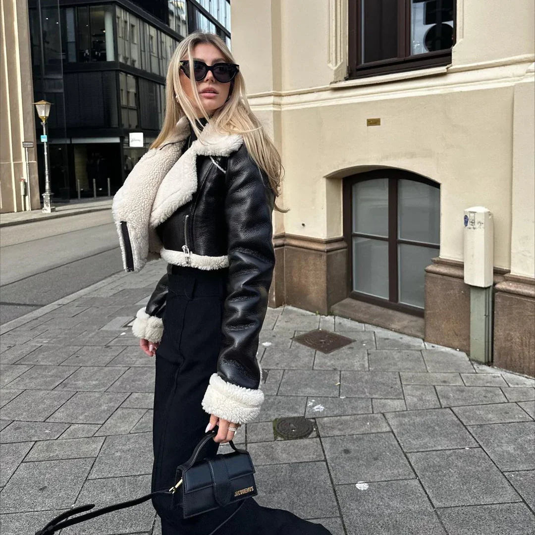 Woman wearing black leather shearling jacket and sunglasses, holding black Jacques purse on city sidewalk