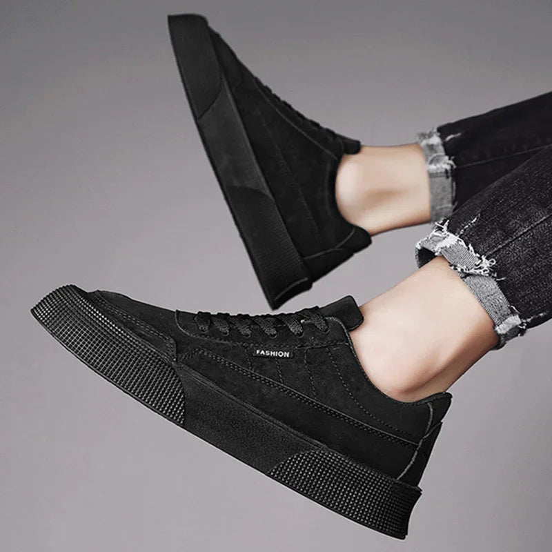 black fashion sneakers with thick rubber soles worn with rolled-up black jeans on gray background