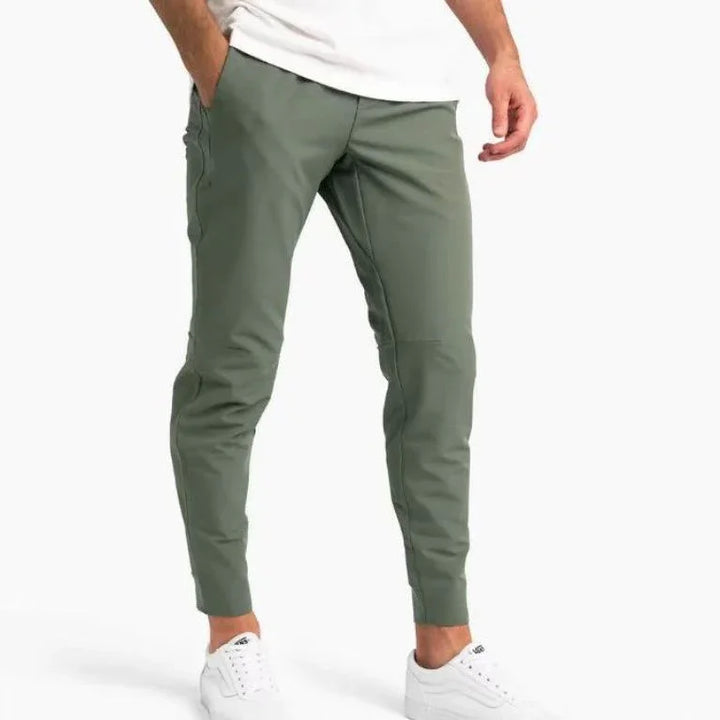 Man wearing slim-fit olive green jogger pants and white sneakers against white background