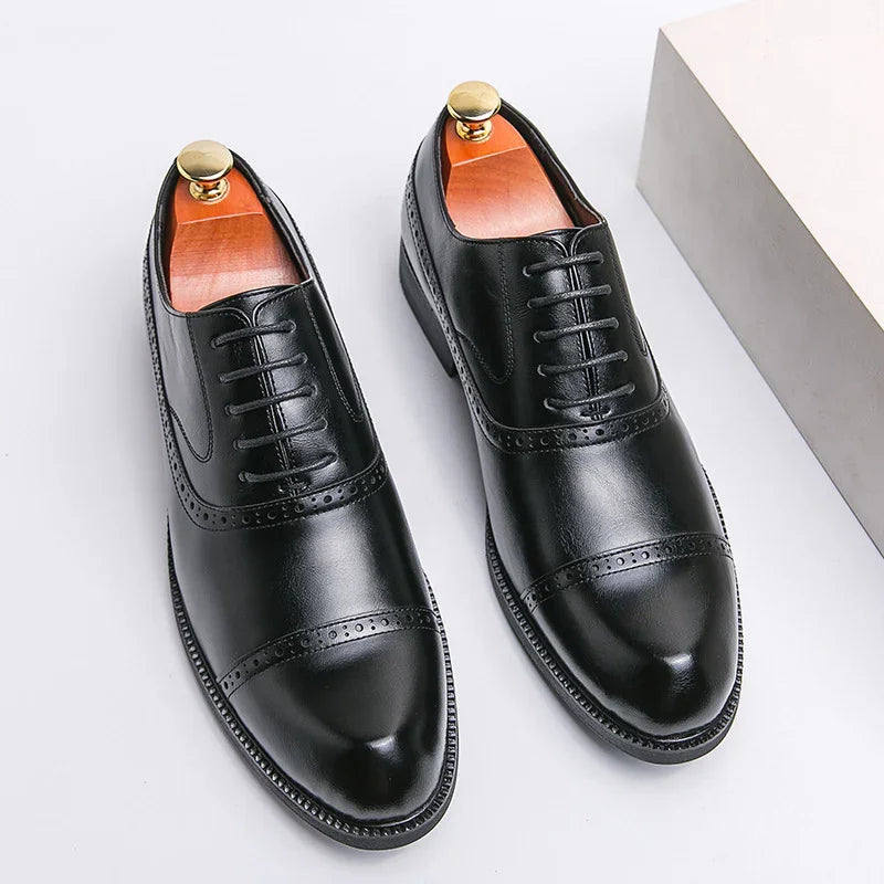 Pair of black leather men's dress shoes with laces and brogue detailing on white surface