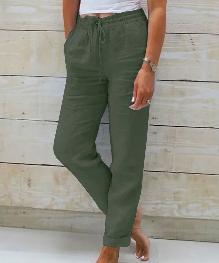 Woman wearing olive green drawstring casual pants standing barefoot against wooden wall