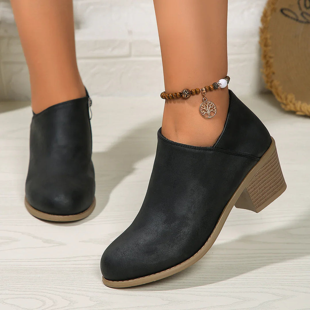 Black leather ankle boots with chunky beige heels worn with a beaded anklet featuring a tree pendant