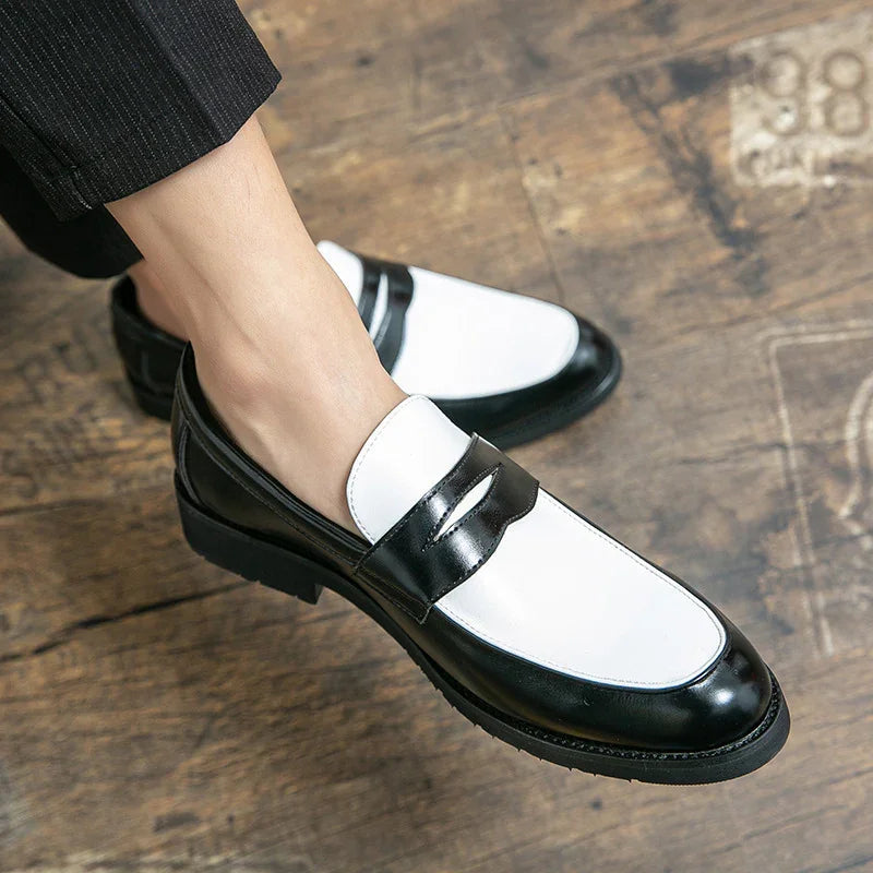 Black and white leather penny loafers on wooden floor, worn with cropped black pants