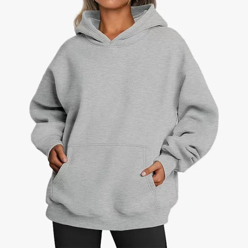 woman wearing oversized light gray hoodie with front pocket and black leggings on white background