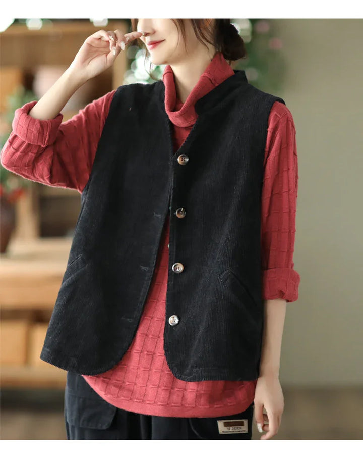 Woman wearing black buttoned corduroy vest over red textured long sleeve shirt in casual indoor setting