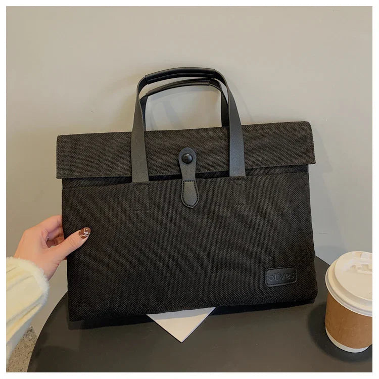 Black textured fabric briefcase with leather handles and clasp on a table next to a coffee cup