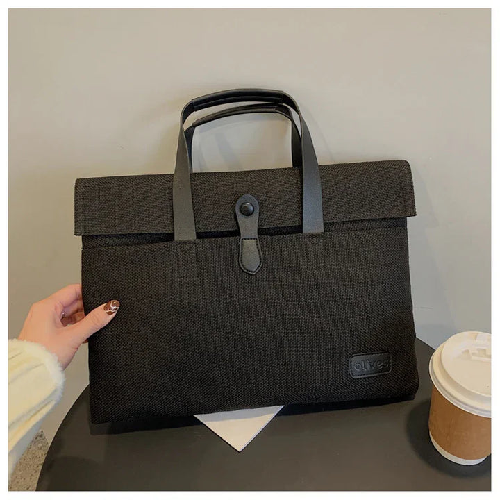 Black textured fabric briefcase with leather handles and clasp on a table next to a coffee cup