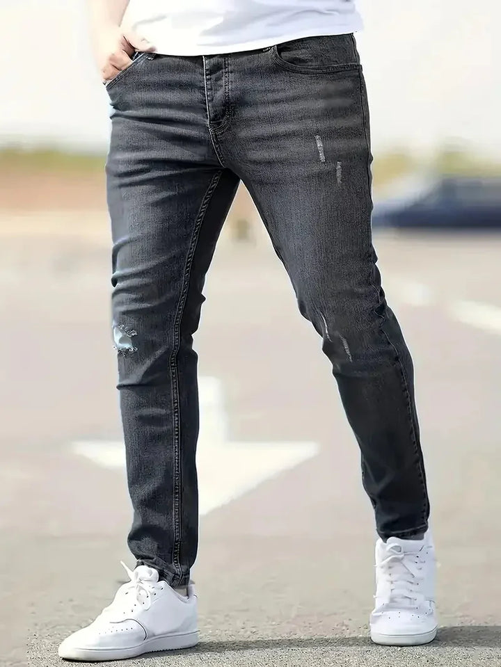 mans legs wearing slim fit distressed black jeans and white sneakers outdoors