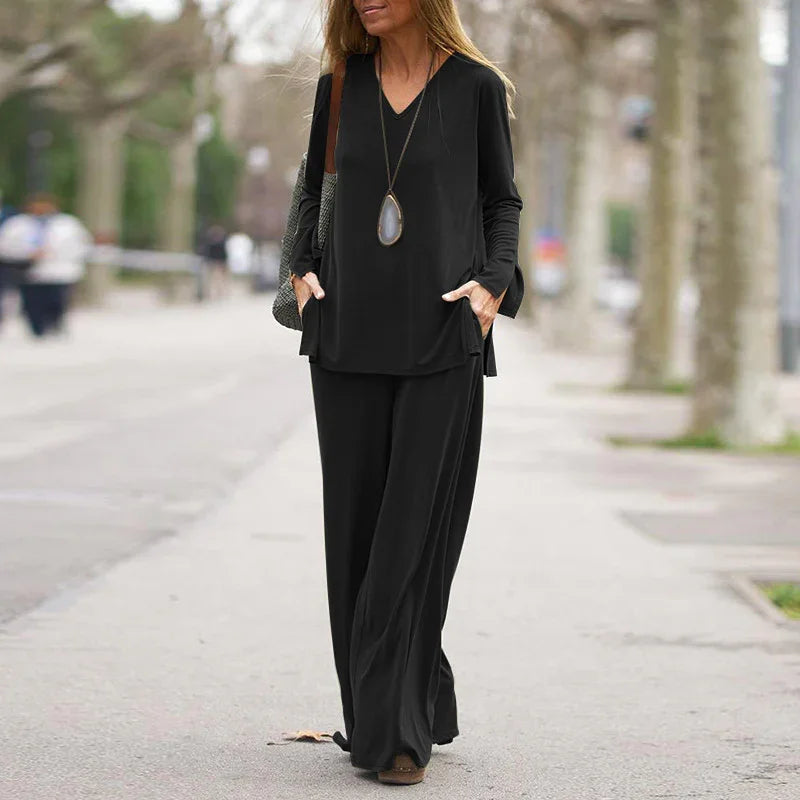 Woman walking outdoors in black long-sleeve V-neck top and wide-leg pants with pendant necklace